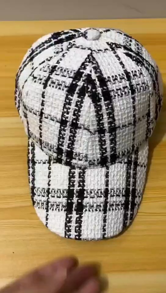White cap with bold black plaid, showing the rounded crown and curved brim from an angled view.