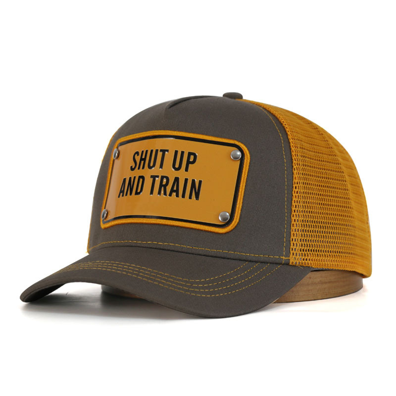 Angled view of a brown trucker hat showing mustard mesh panels, a yellow slogan badge and curved brim.