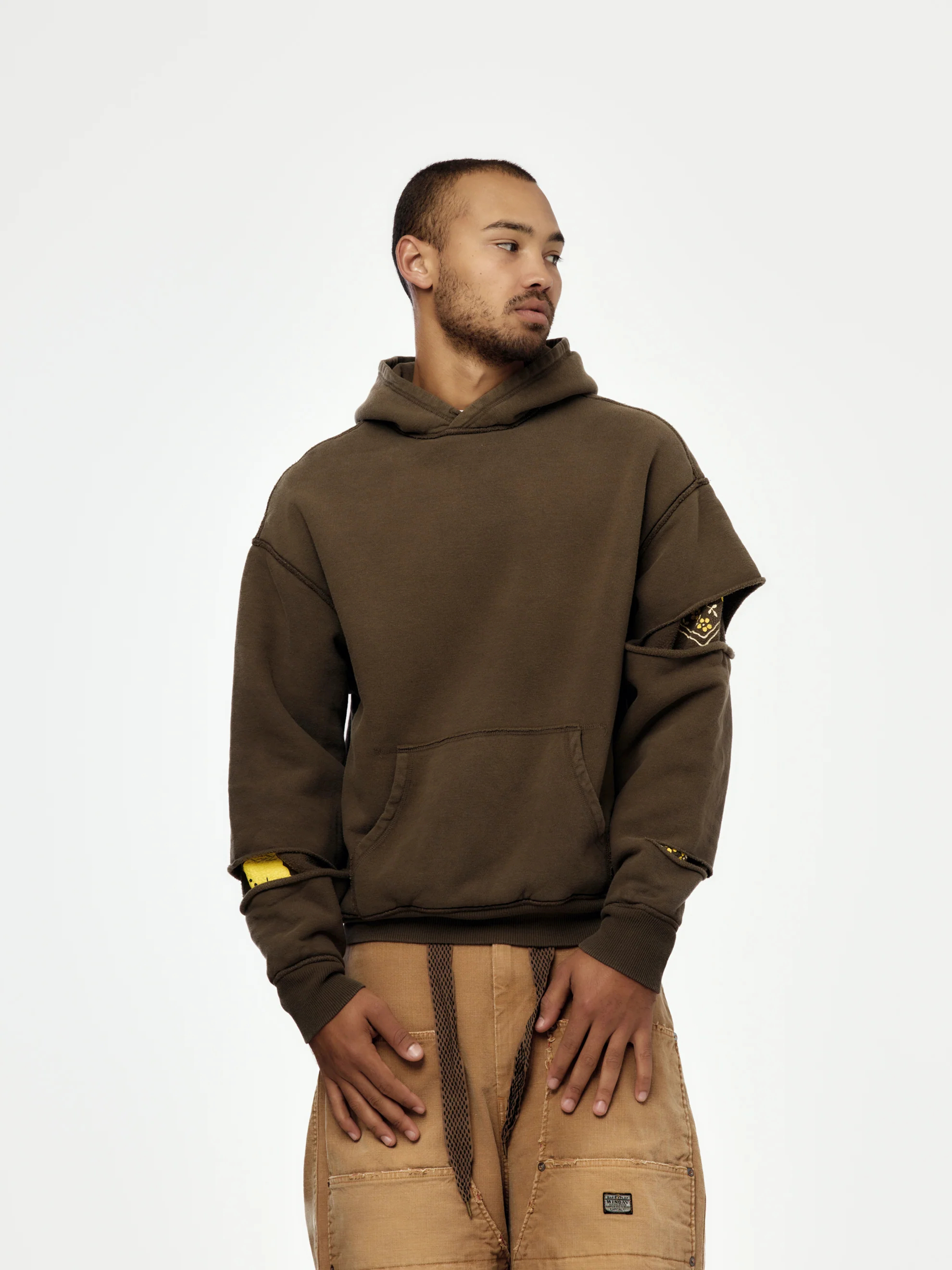 سترة صوفية بنية اللون للجنسين، مصنوعة من نسيج محبوك 460 جرامًا للمتر المربع، قابلة للعكس، ذات تصميم ممزق عند الكوع، مزودة بغطاء رأس وتفاصيل رسومية. 1