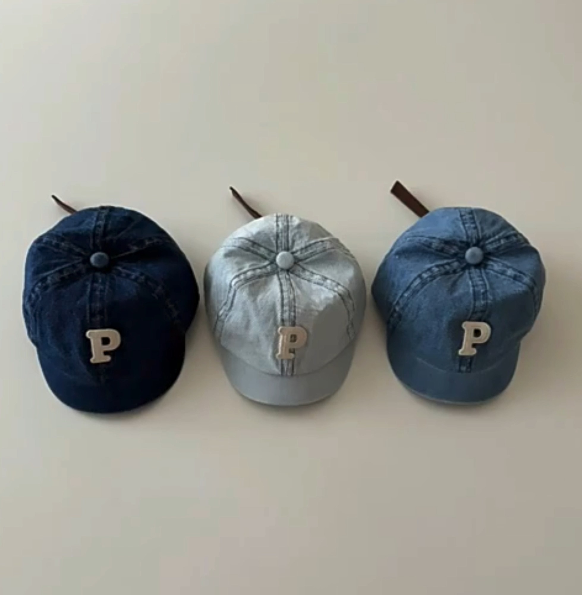 Three denim baby caps in dark, light and medium blue with P letter decorations