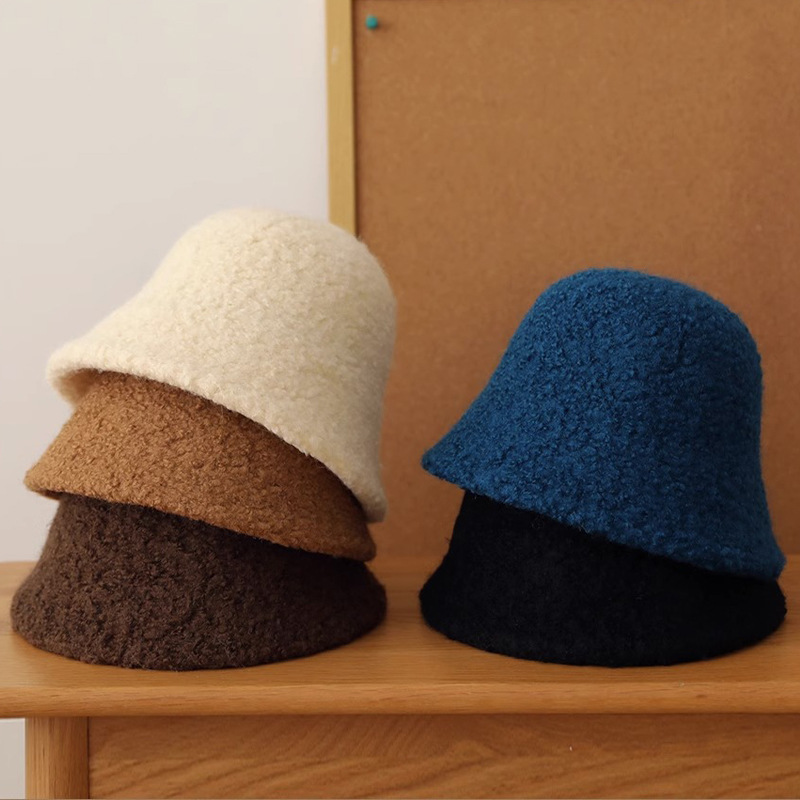 Textured bucket hats in cream, tan, dark brown, blue and black stacked on a wooden shelf.