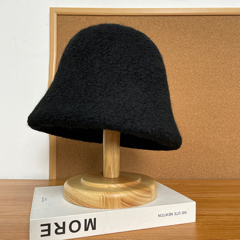 Black bucket hat with a textured surface and downturned brim on a wooden stand.