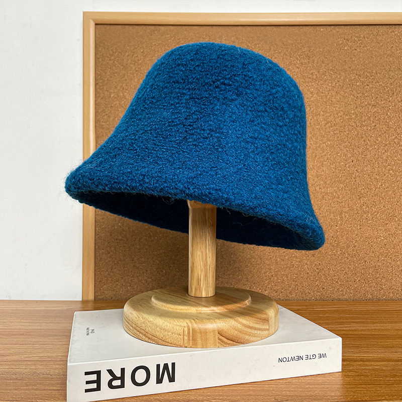 Blue textured bucket hat with a rounded crown and downturned brim on a wooden stand.