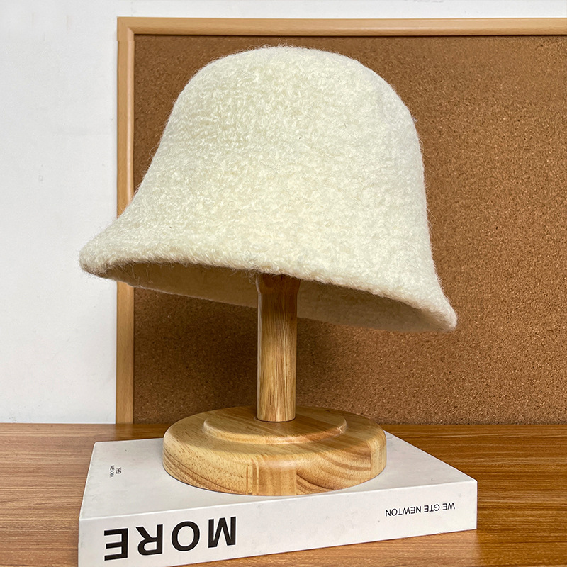 Cream bucket hat with a textured surface and downturned brim on a wooden display stand.