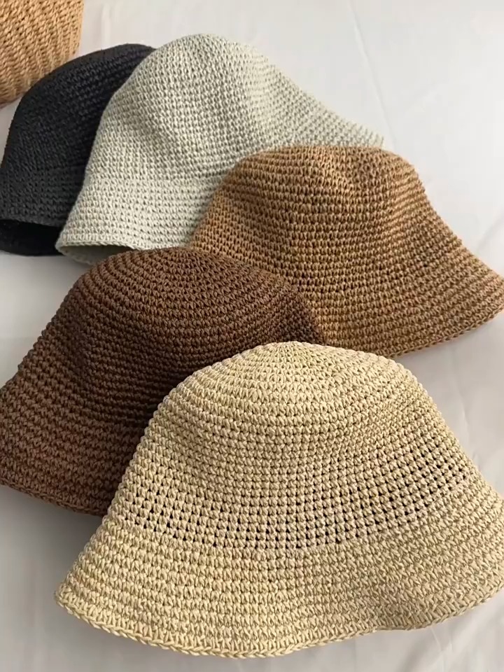 Hands lift and turn woven bucket hats to show their inner bands, fold the crowns and brims, and arrange several colors together