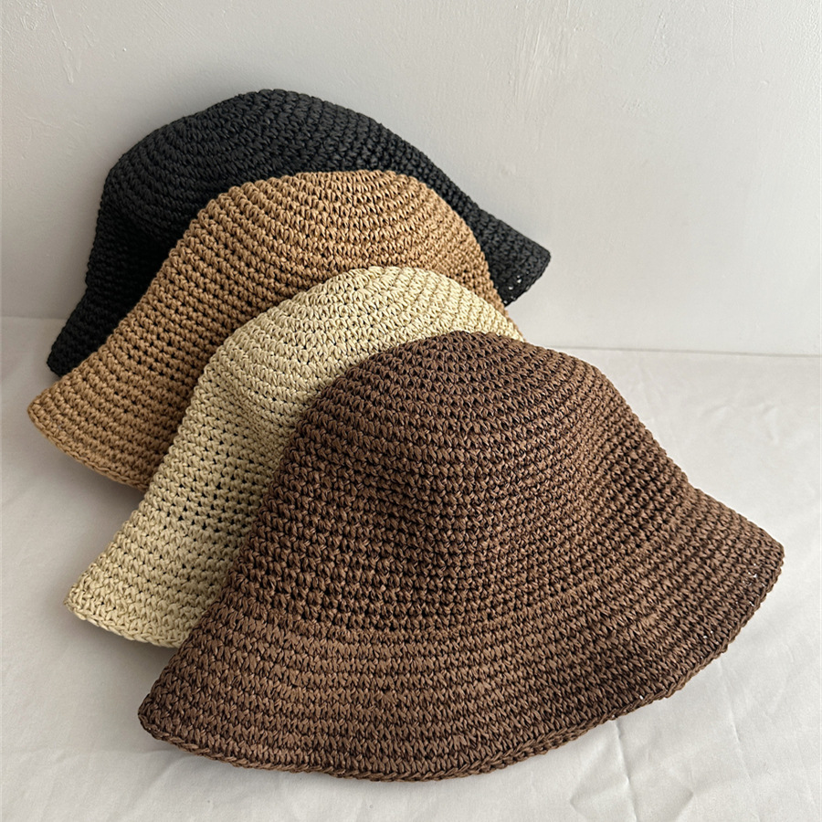 Overhead view of five woven bucket hats with beige and black hats in the foreground