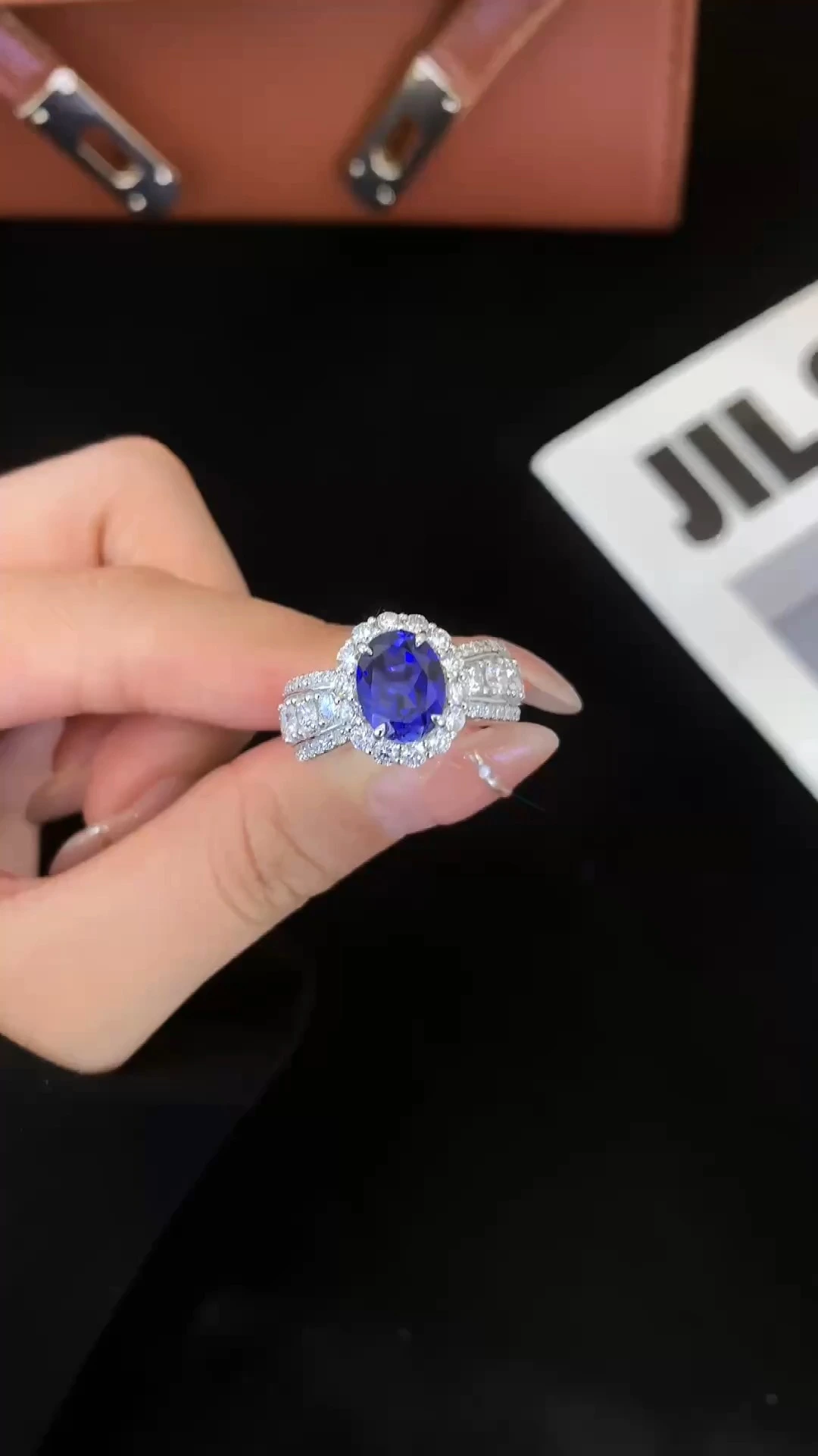 خاتم زفاف من الذهب الأبيض عيار 9 قيراط بيضاوي الشكل بحافة من الدانتيل الفرنسي بتصميم رومانسي، مرصع بحجر ياقوت أزرق مقلد، وزنه 2.52 قيراط، مناسب للذكرى السنوية 1